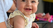Leilani joined the competition — help win amazing prizes! baby, child, smile, face, person, infant, happy, skin, hair, arm, clothing, sleeveless, adult, holding, indoor, blurred_background, closeup, portrait, cute, expression