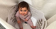 Leilani is registered to the contest to win money with this photo: baby, child, laundry_basket, floor, curious, happy, indoors, fabric, clothing, person, sitting, looking_up, cute, playful, smiling, young_child, home, basket, infant, soft_lighting