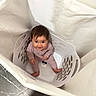 baby, child, laundry_basket, floor, curious, happy, indoors, fabric, clothing, person, sitting, looking_up, cute, playful, smiling, young_child, home, basket, infant, soft_lighting