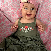 Leilani joined the competition — help win amazing prizes! accessory, apparel, baby, child, closeup, cute, dress, flower, green_dress, happy, headband, indoors, infant, patterned_blanket, person, pink_headband, portrait, sitting, smiling, young_child