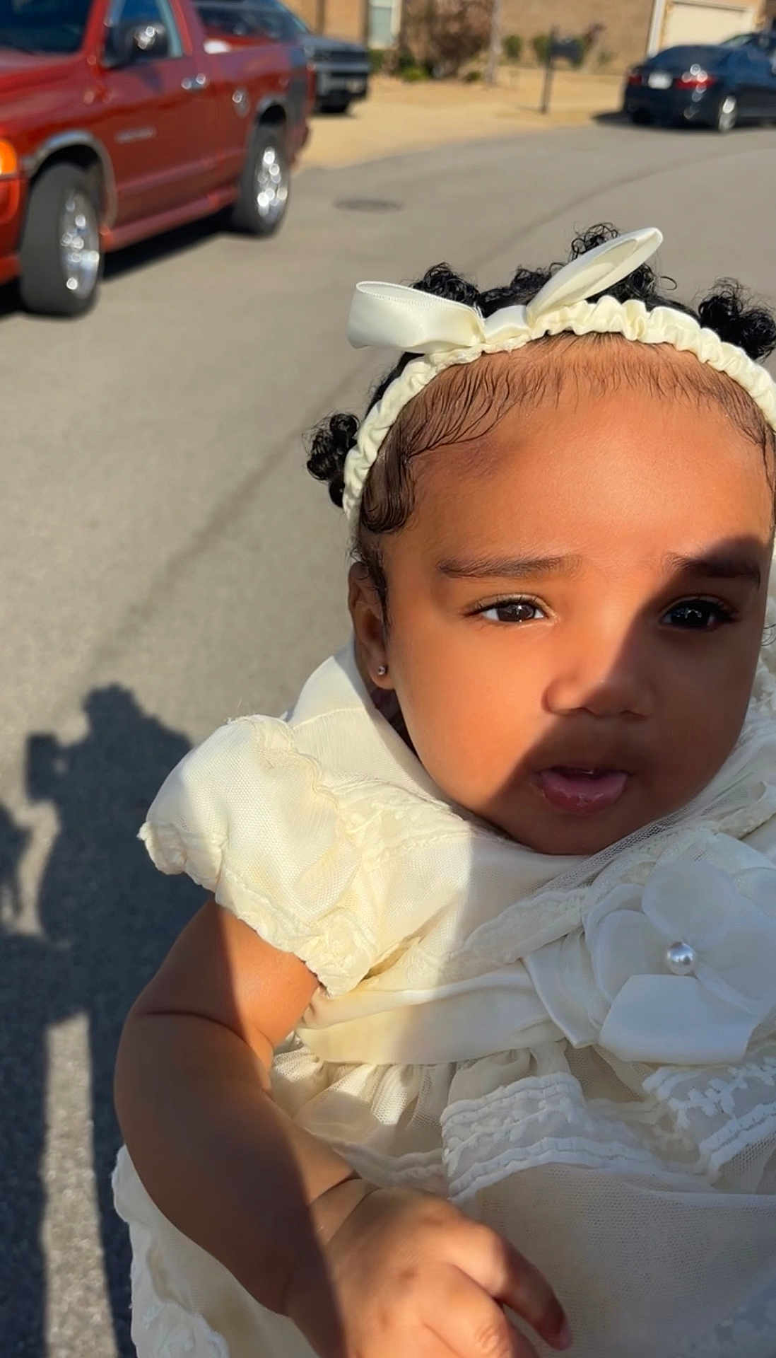 Chozyn is registered to the contest to win money with this photo: toddler, child, outdoor, sunlight, shadow, white_dress, headband, curly_hair, portrait, baby, cute, person, street, vehicle, red_truck, earrings, expression, skin, hand, daytime