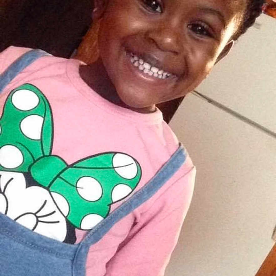 Aundrianna joined the competition — help win amazing prizes! child, girl, smiling, portrait, indoor, pink_shirt, denim_overalls, minnie_mouse, bow, braids, dark_skin, happy, standing, leaning, home, refrigerator, wooden_floor, casual_clothing, photograph, face