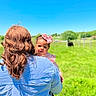 baby, blue_sky, bow, child, cow, curly_hair, daylight, field, grass, greenery, headband, holding, nature, outdoor, pasture, person, portrait, striped_shirt, sunny, woman