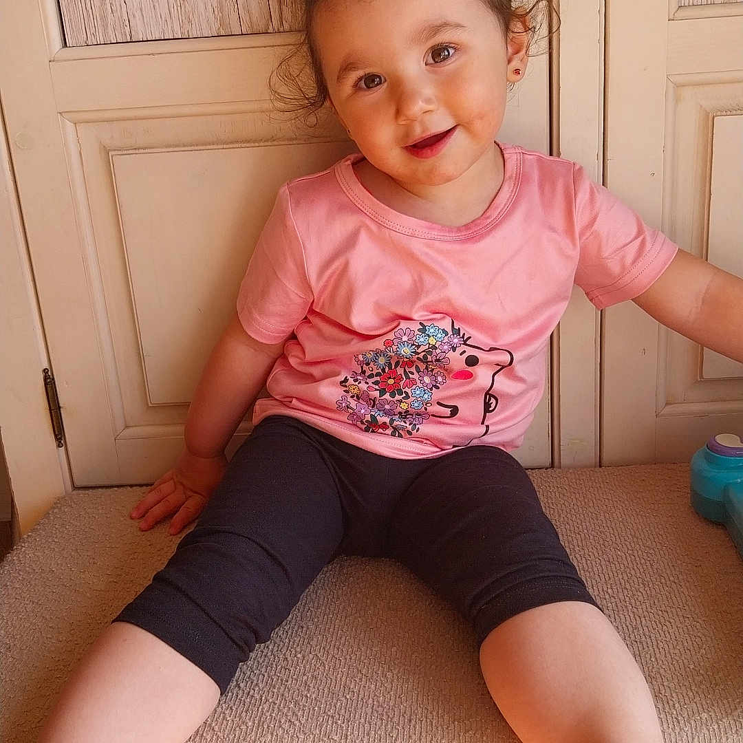 Giulia participe au concours pour gagner de l'argent avec cette photo : black_leggings, carpeted_steps, child, curly_hair, cute, earrings, face, floral_design, happy, home, indoor, person, pink_tshirt, playful, portrait, sitting, smiling, toddler, white_sandals, young_child