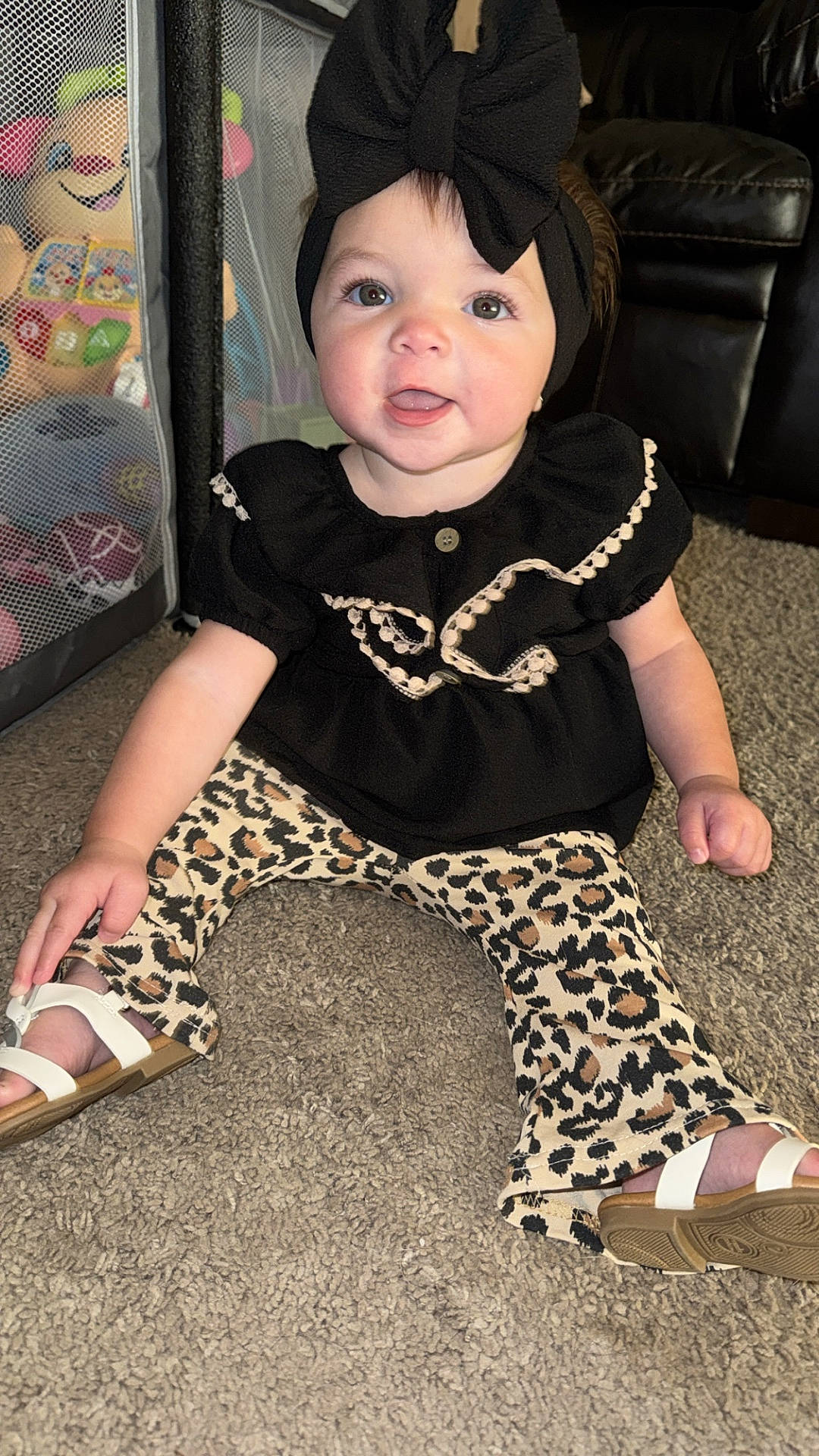 Emerie joined the competition — help win amazing prizes! baby, black_bow, carpet, child, dress, eyes, face, fashion, furniture, happy, indoor, leopard_print, pants, photography, playpen, portrait, sandals, sitting, smiling, toy