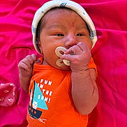 Ismael joined the competition — help win amazing prizes! baby, infant, pacifier, hat, orange_clothing, sailboat_design, pink_blanket, hand, face, newborn, cute, sleepwear, child, lying_down, indoors, soft_texture, calm, small_hands, headwear, fabric