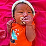 baby, infant, pacifier, hat, orange_clothing, sailboat_design, pink_blanket, hand, face, newborn, cute, sleepwear, child, lying_down, indoors, soft_texture, calm, small_hands, headwear, fabric