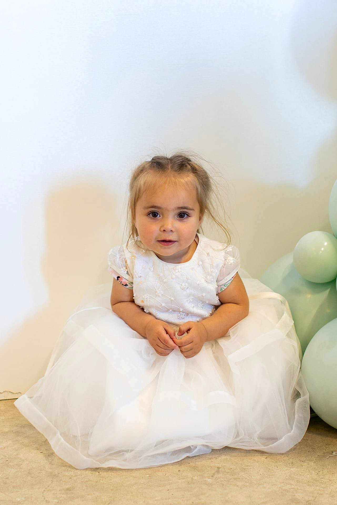 Giulia participe au concours pour gagner de l'argent avec cette photo : baby, baby_toddler_clothing, balloon, blond, bridal_accessory, child, dress, event, flash_photography, flooring, formal_wear, fun, gesture, happy, jewellery, person, portrait_photography, room, sitting, skin