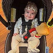 Mavis is registered to the contest to win money with this photo: baby, baby_accessories, car_seat, child, comfort, cute, happy, hat, headwear, indoors, infant, pacifier, pajamas, patterned_clothing, plush_toy, safety, seatbelt, smiling, wooden_floor, young_child