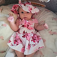 Paisley joined the competition — help win amazing prizes! baby, infant, dress, hat, floral_pattern, pink, white, blanket, plush_toys, soft_toy, cute, lying_down, raised_fist, indoors, comfort, child, adorable, face, person, clothing