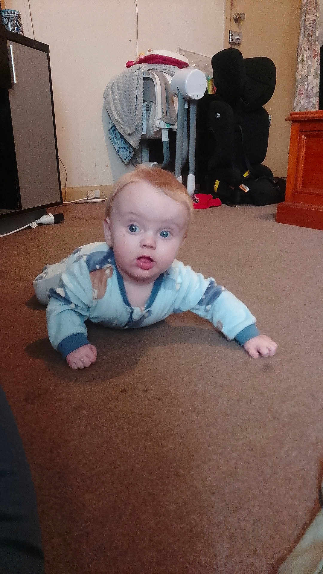 Zachariah is registered to the contest to win money with this photo: baby, carpet, pajamas, child, indoor, floor, car_seat, high_chair, furniture, curtains, door, cabinet, expression, wide_eyes, curious, person, young_child, room, home, toy