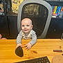 baby, child, desk, computer_mouse, keyboard, office_chair, lego, bookshelf, books, games, toy, indoor, curious, smiling, person, table, furniture, striped_clothing, overalls, home_office