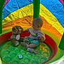 Oliver is registered to the contest to win money with this photo: baby, child, inflatable_pool, toy, plush_dog, pacifier, rainbow, colorful, playtime, sitting, infant, cute, indoors, plastic, clothing, shorts, tshirt, foot, hand, summer