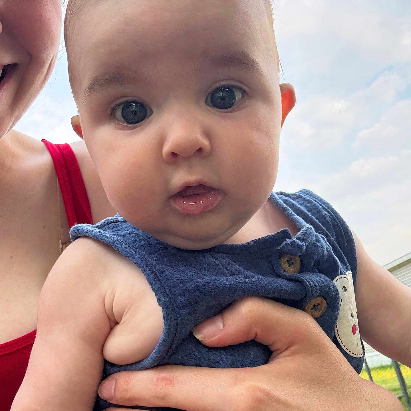 Kienna joined the competition — help win amazing prizes! adult_hand, baby, blue_clothing, button, child, clouds, cute, expression, eyes, face, holding, infant, mouth, outdoor, person, portrait, red_clothing, skin, sky, smile