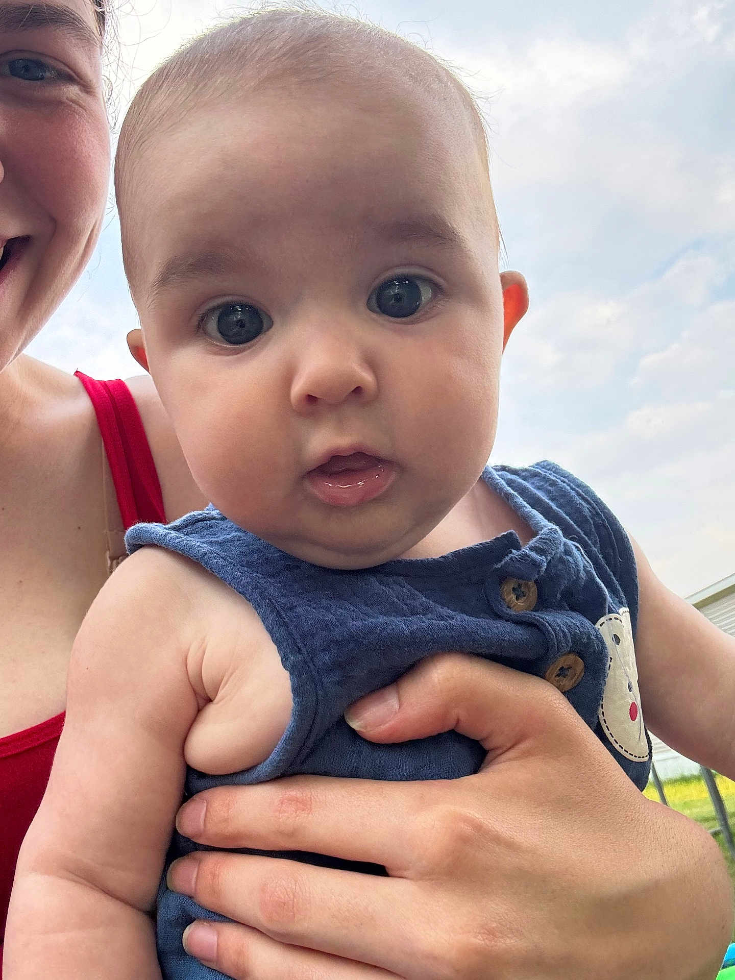 Kienna joined the competition — help win amazing prizes! baby, infant, child, person, adult_hand, smile, face, blue_clothing, red_clothing, outdoor, sky, clouds, cute, portrait, holding, skin, expression, eyes, mouth, button
