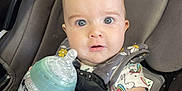 Kienna is registered to the contest to win money with this photo: baby, milk_bottle, car_seat, graco, infant, child, seatbelt, unicorn_pattern, clothing, hand, face, eyes, expression, car_interior, seat, feeding, milk, plastic, safety, closeup