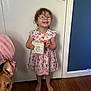 child, girl, glasses, dress, floral, barefoot, wooden_floor, door, dog, pet, indoor, sign, smiling, happy, holding, curly_hair, pink, home, cute, person