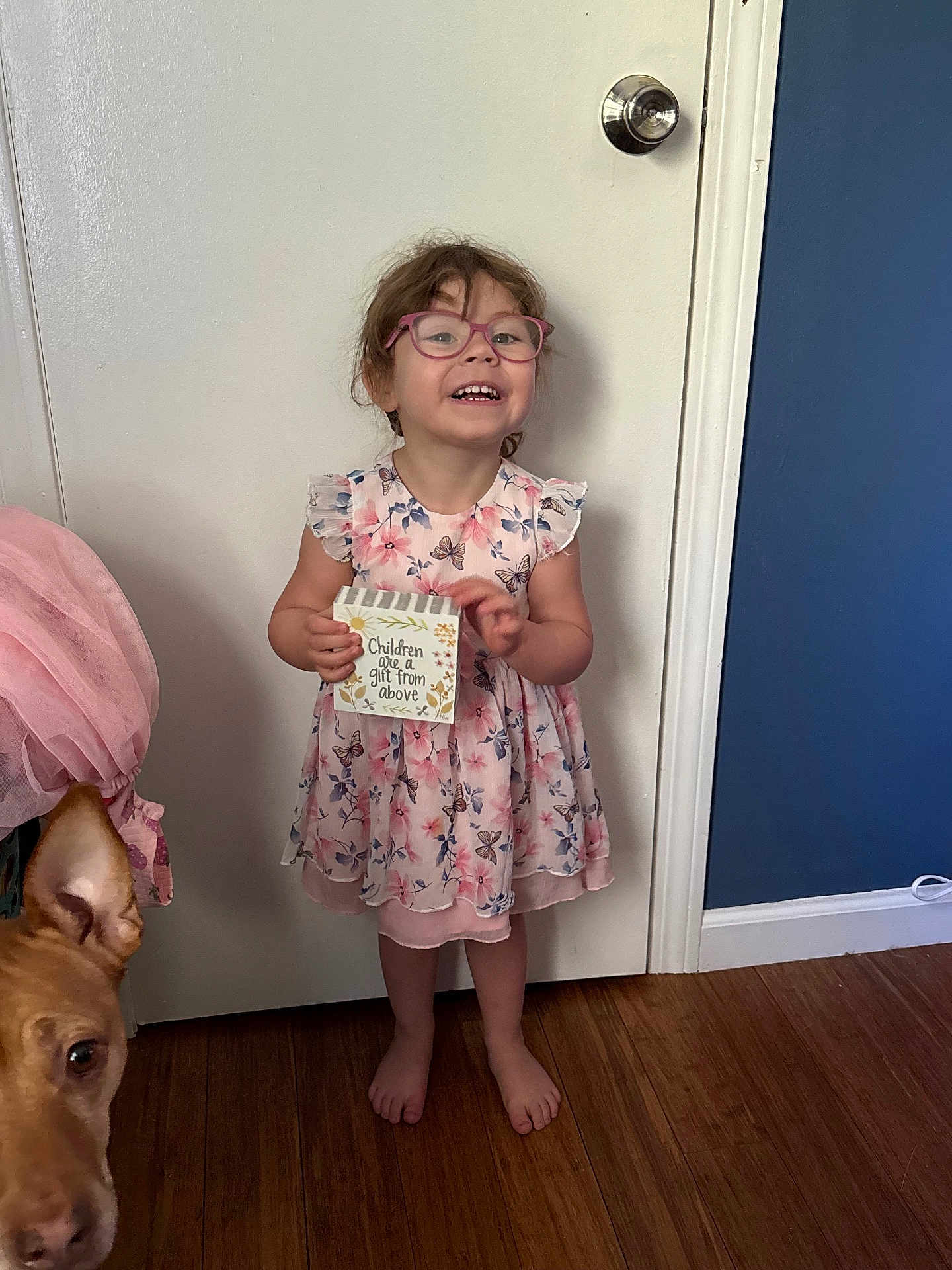 Aradhana joined the competition — help win amazing prizes! child, girl, glasses, dress, floral, barefoot, wooden_floor, door, dog, pet, indoor, sign, smiling, happy, holding, curly_hair, pink, home, cute, person