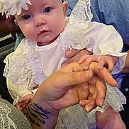 Octavia is registered to the contest to win money with this photo: baby, infant, child, white_clothing, lace, headband, flower, hand, adult_hand, holding, curious, blue_eyes, portrait, indoor, seated, person, cute, soft_lighting, closeup, fabric