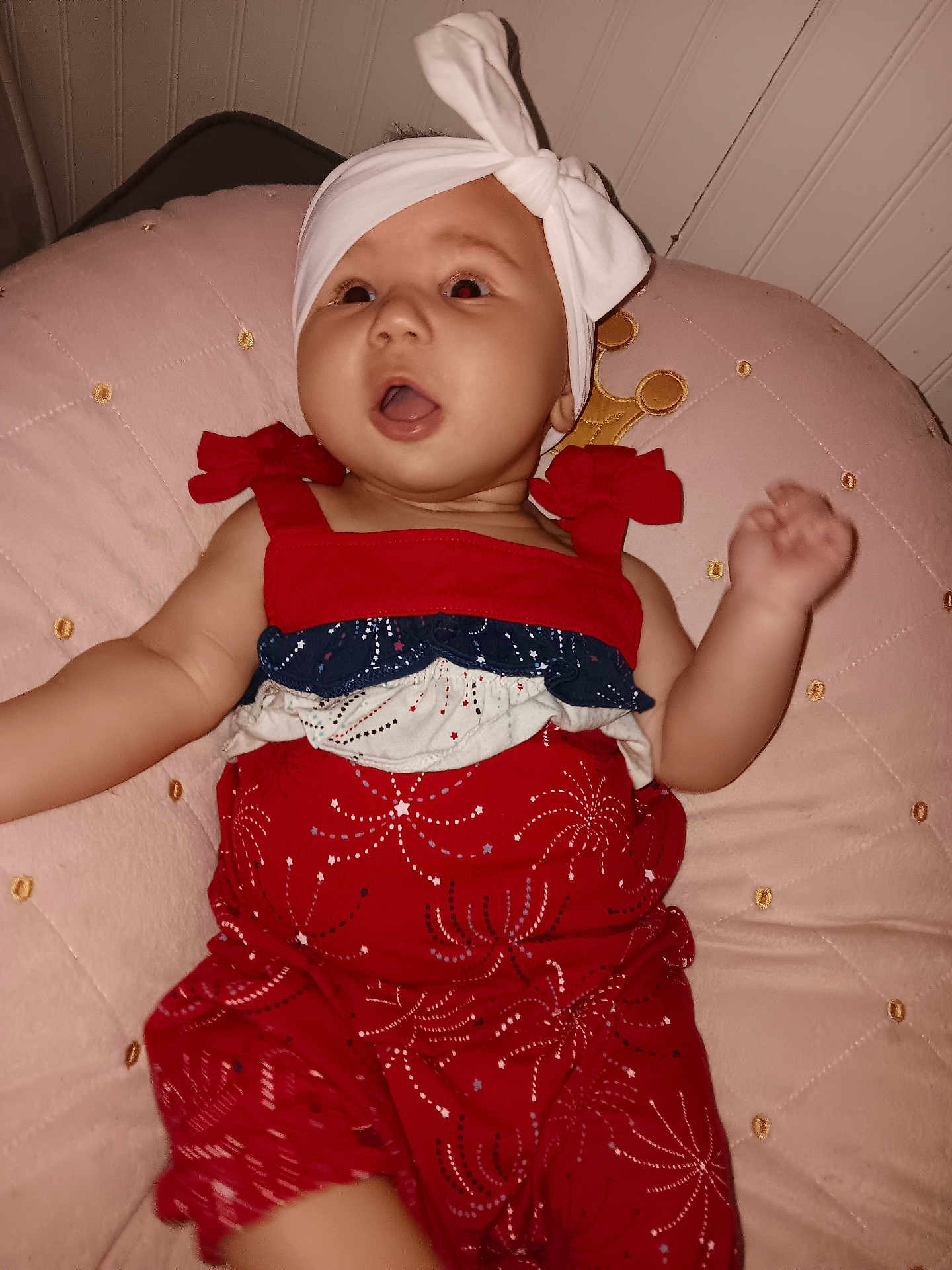 Luna is registered to the contest to win money with this photo: baby, infant, child, red_outfit, headband, white_bow, pink_cushion, expression, mouth_open, indoor, cute, soft_furniture, person, portrait, celebration, patterned_clothing, happy, small_child, lying_down, closeup