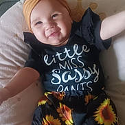 Luna joined the competition — help win amazing prizes! baby, baby_girl, black_clothing, child, comfortable, cushion, cute, face, fashion, happy, headband, indoor, infant, person, portrait, sitting, smiling, sunflower_pattern, yellow, young_child