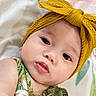 baby, infant, child, portrait, close_up, face, eyes, smiling, lying_down, headband, bow, mustard, green_outfit, patterned_clothing, floral_blanket, bed, indoor, baby_fashion, cute, photography