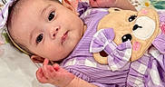 Celia joined the competition — help win amazing prizes! baby, infant, child, portrait, lying_down, purple_outfit, dress, bow, headband, teddy_bear, stuffed_animal, floral_bedding, bed, indoors, wide_eyes, smiling, hands, arms, close_up, colorful