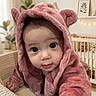 baby, child, infant, portrait, pink_hood, hooded_outfit, cute, wide_eyed, sitting, indoor, nursery, crib, stuffed_animals, teddy_bear, plant, wall_art, fairy_lights, furniture, cozy, close_up