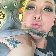 Bella joined the competition — help win amazing prizes! sphynx_cat, cat, hairless_cat, person, selfie, tattoo, nose_ring, makeup, false_eyelashes, puckered_lips, arm, hand, indoor, ceiling_light, kitchen, countertop, close_up, pet_owner, wide_eyes, skin_texture