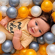 Ilaria is registered to the contest to win money with this photo: baby, baby_clothing, ball_pit, blue_eyes, child, close_up, face, gray_balls, hair, hands, happy, infant, onesie, plastic_balls, playful, portrait, smiling, toy, white_balls, yellow_balls
