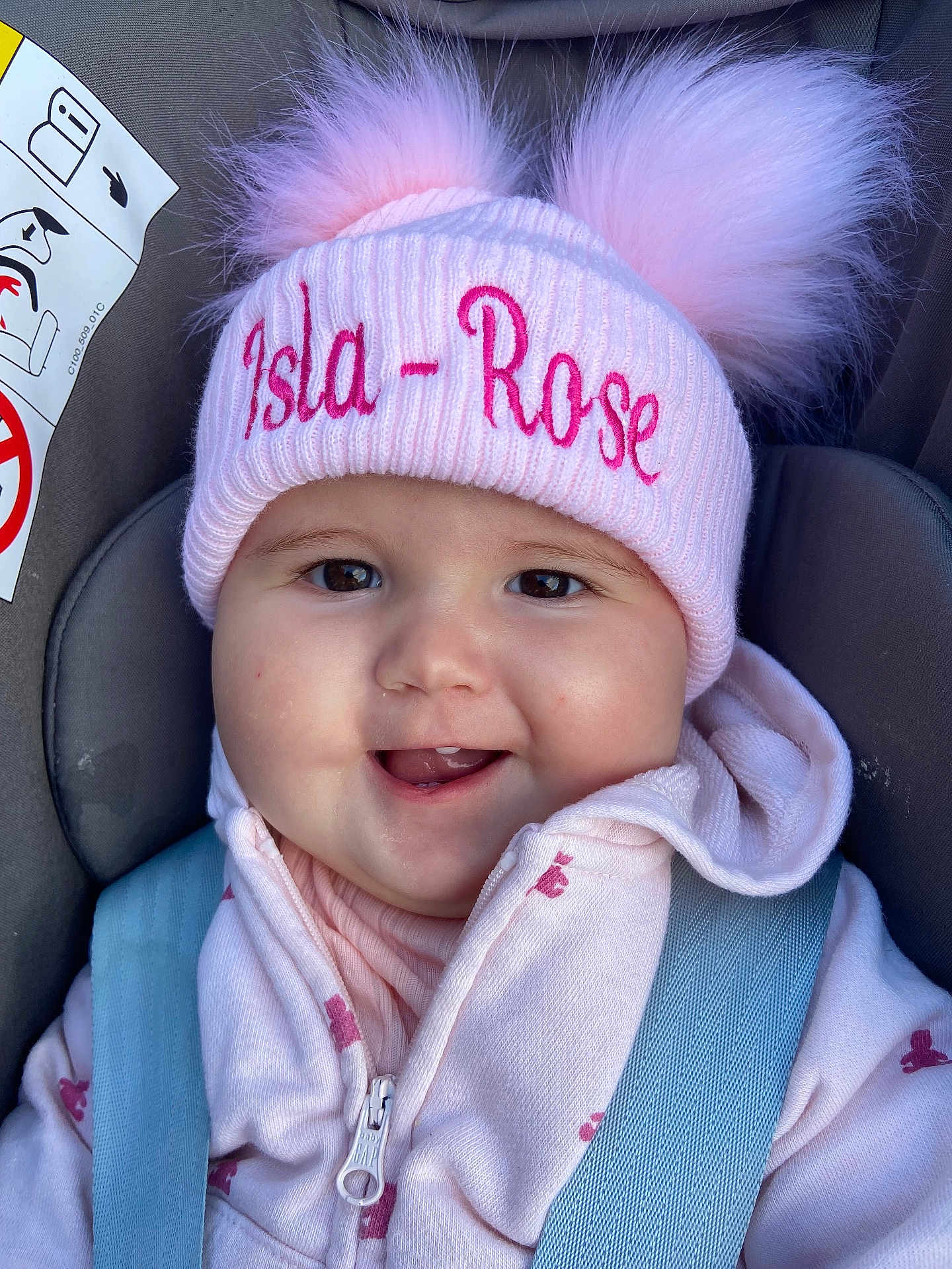 Isla-Rose is registered to the contest to win money with this photo: baby, car_seat, child, childrens_fashion, closeup, clothing, cute, face, happy, headwear, hoodie, infant, pink_hat, pom_pom, portrait, seatbelt, smiling, warm_clothes, young_child, zipper