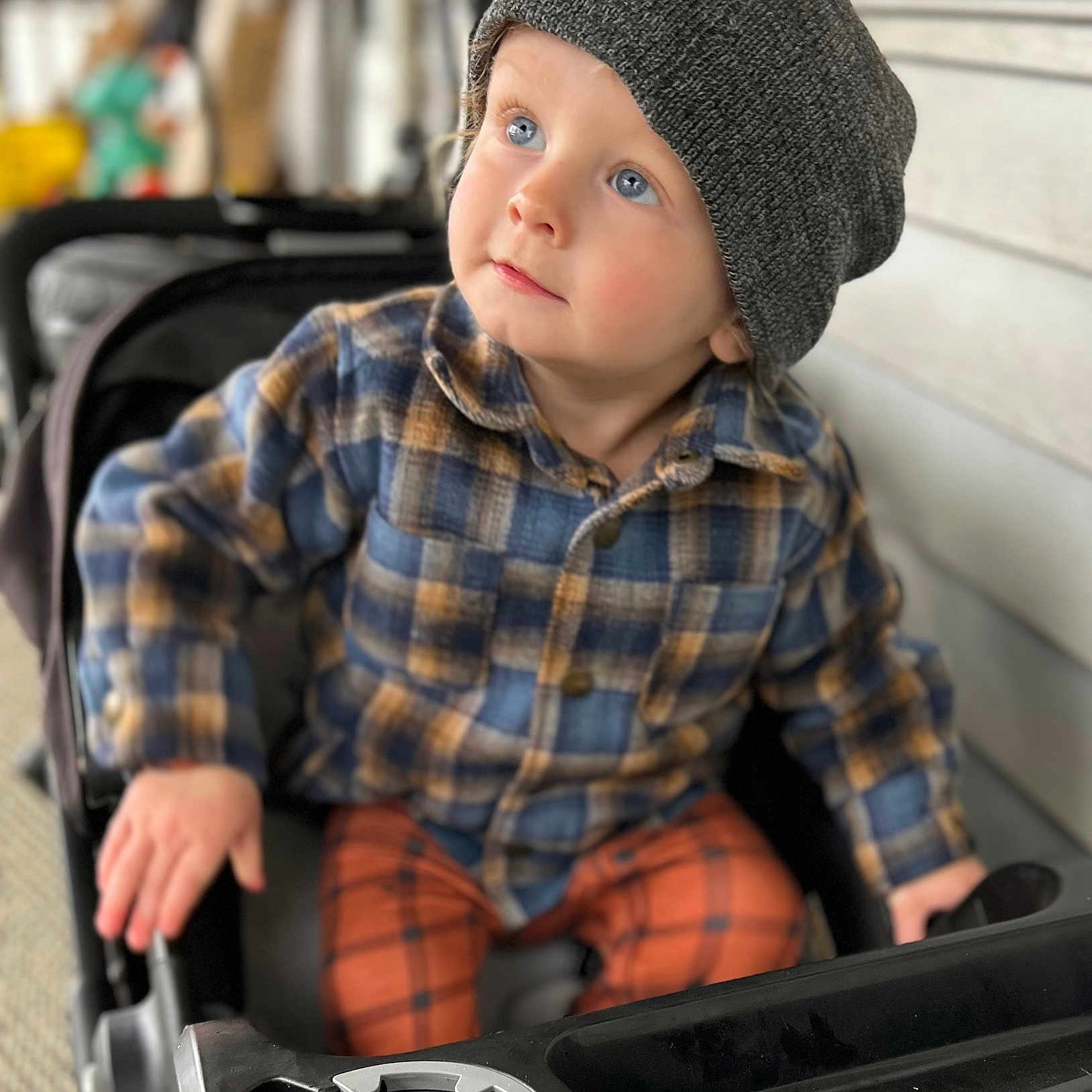 Raylan joined the competition — help win amazing prizes! beanie, blue_eyes, casual_wear, child, closeup, curious, cute, face, hands, headwear, indoor, person, plaid_shirt, portrait, seated, soft_lighting, stroller, toddler, warm_clothing, young_child