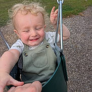 Raylan joined the competition — help win amazing prizes! toddler, child, swing, playground, smile, happy, blonde_hair, curly_hair, holding_hands, outdoor, grass, wood_chips, green_swing, metal_chain, short_sleeve_shirt, overalls, person, daylight, fun, park