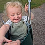 toddler, child, swing, playground, smile, happy, blonde_hair, curly_hair, holding_hands, outdoor, grass, wood_chips, green_swing, metal_chain, short_sleeve_shirt, overalls, person, daylight, fun, park