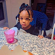 Siki Nelsia a rejoint le concours — aidez-le/la à gagner de superbes lots ! beads, braided_hair, casual, child, curious, cute, food, girl, granite_countertop, home, indoor, kitchen, pastry, person, pink_cup, portrait, seated, snack, table, young