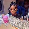 beads, braided_hair, casual, child, curious, cute, food, girl, granite_countertop, home, indoor, kitchen, pastry, person, pink_cup, portrait, seated, snack, table, young