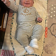 Alessio participe au concours pour gagner de l'argent avec cette photo : baby, infant, smile, lying_down, onesie, striped_clothing, white_shoes, changing_pad, blanket, towel, hand, face, chubby_cheeks, table, tablecloth, heart_pattern, owl_border, home_interior, wooden_floor, adorable