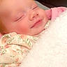 baby, sleeping, blanket, floral_clothing, smile, cozy, infant, face, peaceful, cute, soft_texture, indoors, child, comfort, resting, closeup, warmth, pink, white, adorable