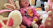 Elena is registered to the contest to win money with this photo: baby, plush_toy, bunny, pink_clothing, quilted_blanket, smiling, indoor, soft_toy, child, stuffed_animal, gnome, living_room, tissue_box, decor, portrait, cute, seated, toy, happy, furniture