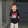 Cuauhtemoc joined the competition — help win amazing prizes! child, boy, smiling, standing, black_tshirt, shorts, glass_door, reflection, outdoor, casual_clothing, happy, confident, portrait, young, person, feet, hair_tied, text_on_clothing, daylight, concrete_floor