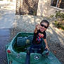 backyard, casual_clothing, child, fence, fun, gesture, gravel, outdoor, person, plant, playful, shadow, spiderman, sunglasses, sunlight, tank, tongue_out, toy, tshirt, window