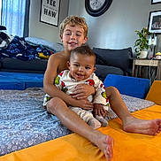 Bentley is registered to the contest to win money with this photo: baby, bed, blanket, casual, child, clock, comfort, cushion, cute, family, happy, home, indoor, living_room, plant, portrait, siblings, smiling, toddler, wall_art