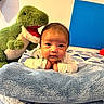 baby, child, infant, portrait, smiling, wide_eyed, lying_down, blanket, bed, plush_toy, dinosaur, stuffed_animal, green, blue, quilt, bedroom, indoors, cozy, photography, close_up