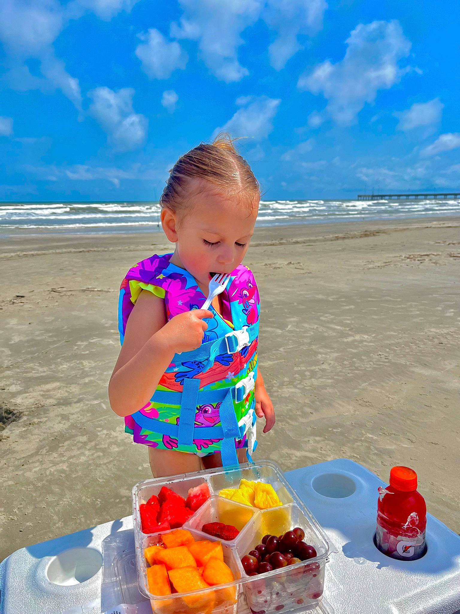 Arabella is registered to the contest to win money with this photo: beach, blue, cloud, fun, holiday, horizon, juice, landscape, leisure, orange_drink, outdoor_furniture, people_on_beach, person, plate, sand, sky, summer, tableware, toddler, travel