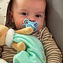baby, pacifier, plush_toy, blanket, striped_clothing, infant, seated, soft_toy, cute, child, indoors, comfort, baby_seat, patterned_fabric, hand, face, head, eyes, mouth, cozy