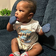 Kevarious joined the competition — help win amazing prizes! baby, child, mittens, socks, couch, clothing, shirt, shorts, indoor, person, cute, sitting, curious, face, head, furniture, home, skin, expression, infant