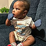 baby, child, mittens, socks, couch, clothing, shirt, shorts, indoor, person, cute, sitting, curious, face, head, furniture, home, skin, expression, infant