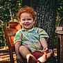 child, toddler, red_hair, curly_hair, smile, bare_feet, chair, outdoor, forest, tree_trunk, patterned_shirt, pineapple_shirt, wooden_furniture, portrait, sunlight, candid, summertime, nature, happy, barefoot