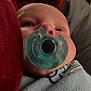 William is registered to the contest to win money with this photo: baby, pacifier, blanket, close_up, face, infant, child, soft_lighting, red_fabric, gray_fabric, portrait, wrapped, young, cute, indoors, comfort, resting, human, skin, expression