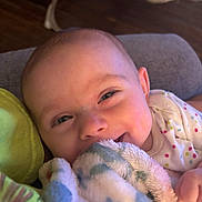 Emma joined the competition — help win amazing prizes! baby, infant, blanket, smile, eyes, onesie, polka_dots, couch, pillow, fuzzy_texture, close_up, happy, lying_down, hand, cheek, soft_lighting, indoor, wooden_floor, baby_seat, portrait